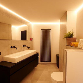 Modernes Badezimmer mit großem Spiegel, Waschbecken, Handtüchern und indirekter Beleuchtung.