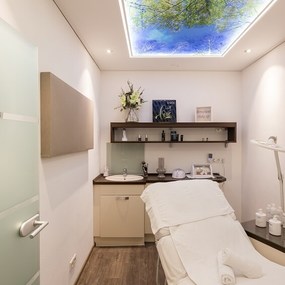 Moderner Behandlungsraum für Kosmetik mit Wellnessliege und Naturmotiv an der Decke.