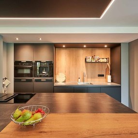 Moderne Einbauküche mit Kochinsel, Obstschale, dunklen Fronten und Holz-Elementen.